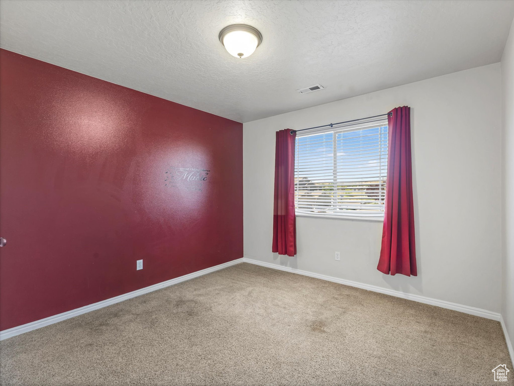 Carpeted empty room featuring a textured ceiling and baseboards