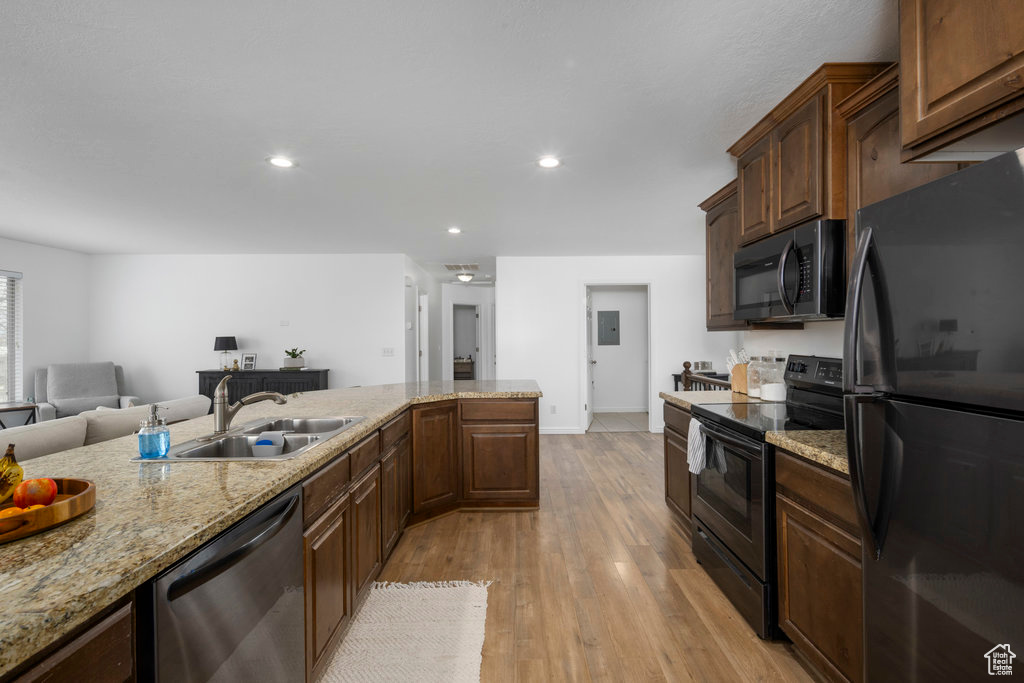 Kitchen with appliances with stainless steel finishes, a sink, light wood-style flooring, light stone countertops, and baseboards