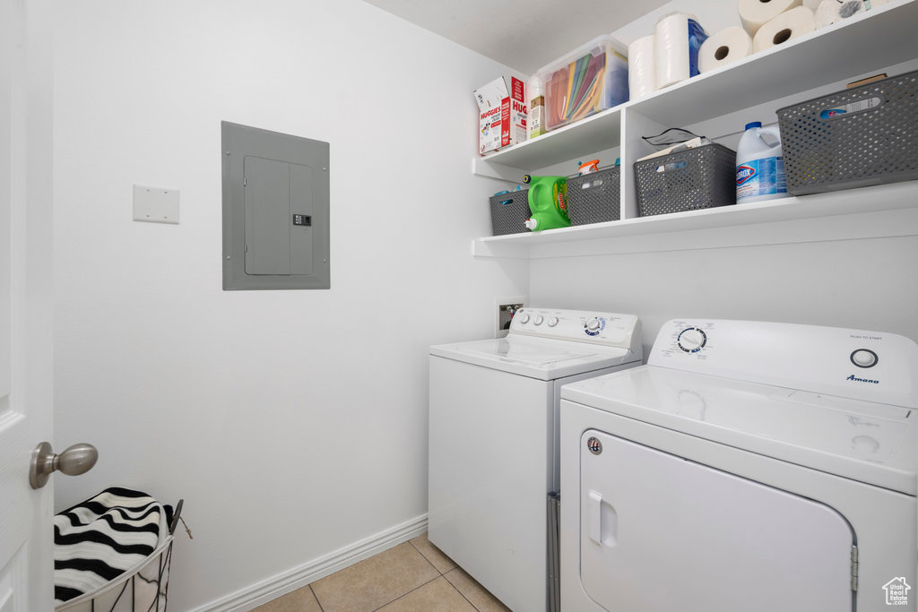 Laundry area with electric panel, washer and dryer, light tile patterned floors, and baseboards