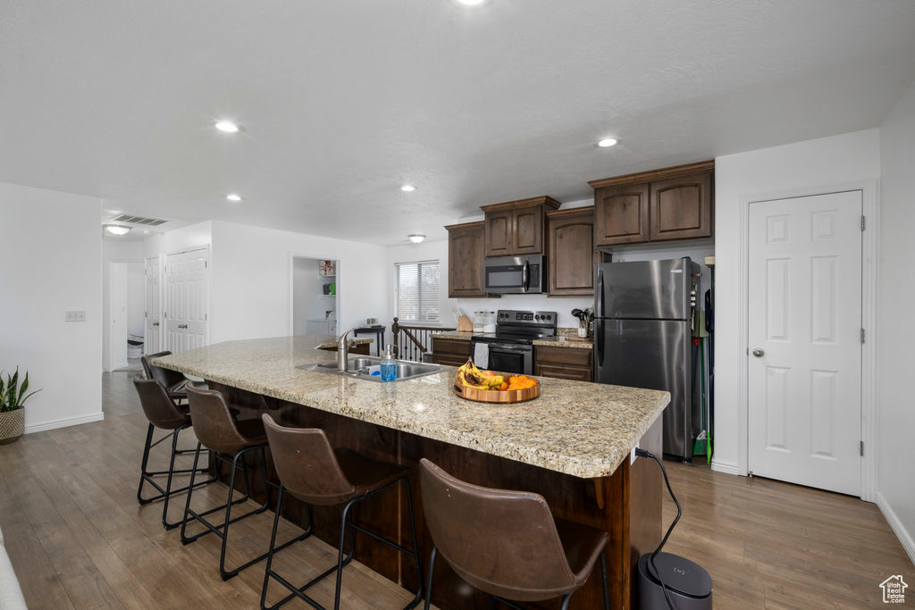 Kitchen featuring stainless steel appliances, a sink, a kitchen island with sink, dark wood-style floors, and a kitchen bar