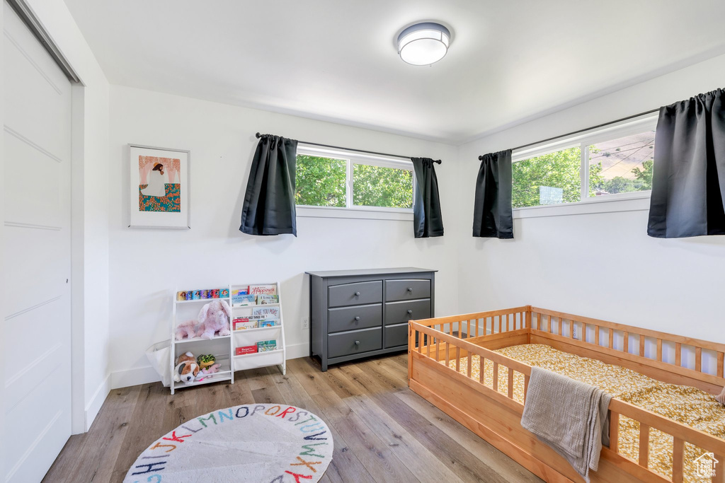 Bedroom with wood finished floors, a nursery area, and baseboards
