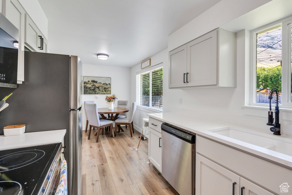 Kitchen featuring dishwasher, a sink, light wood-style floors, light countertops, and electric range oven