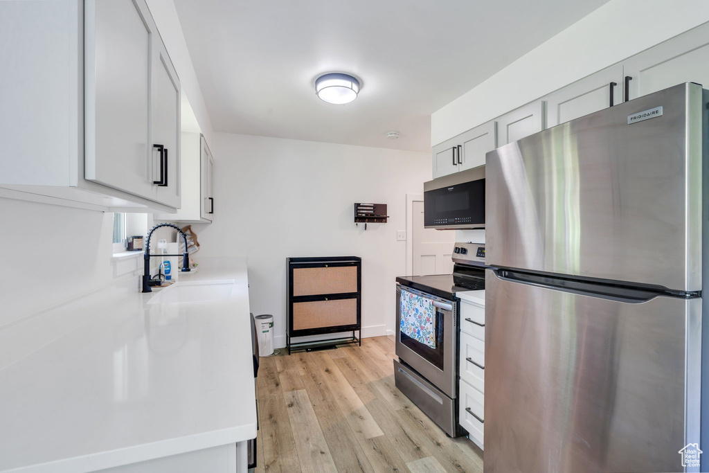 Kitchen with appliances with stainless steel finishes, a sink, light wood-style floors, and light countertops