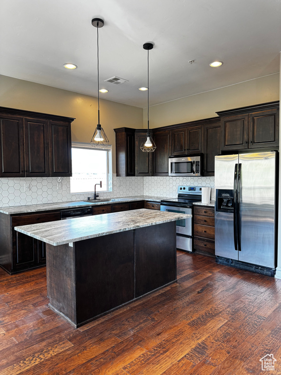 Kitchen with appliances with stainless steel finishes, a sink, a kitchen island, tasteful backsplash, and hanging light fixtures