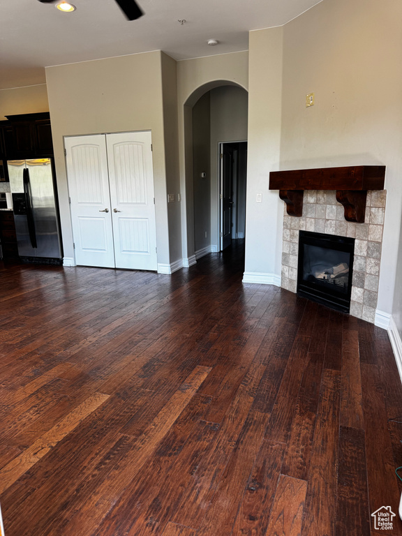Unfurnished living room featuring a stone fireplace, arched walkways, wood finished floors, and baseboards