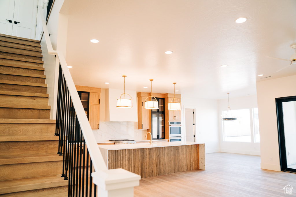 Kitchen with light countertops, stainless steel double oven, a spacious island, light wood-style floors, and recessed lighting