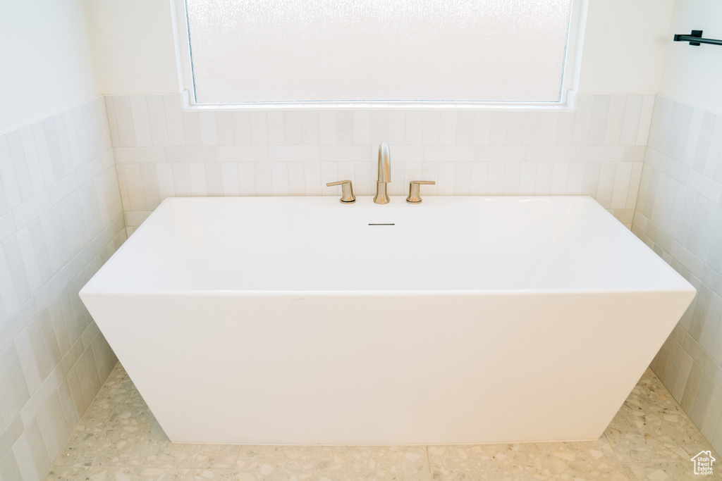 Full bathroom featuring a soaking tub, tile walls, and healthy amount of natural light