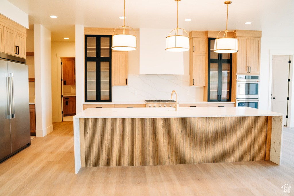 Kitchen featuring stainless steel appliances, light wood-style flooring, light brown cabinetry, a center island with sink, and light countertops