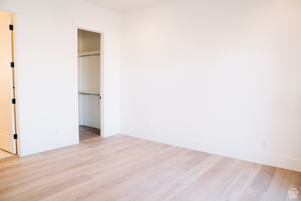 Unfurnished bedroom with light wood finished floors, baseboards, a spacious closet, and a closet