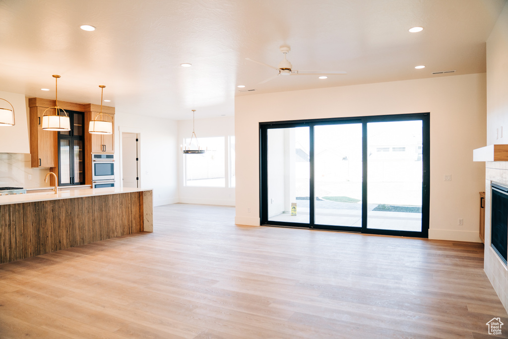 Unfurnished living room with a tiled fireplace, recessed lighting, light wood-style flooring, a sink, and ceiling fan