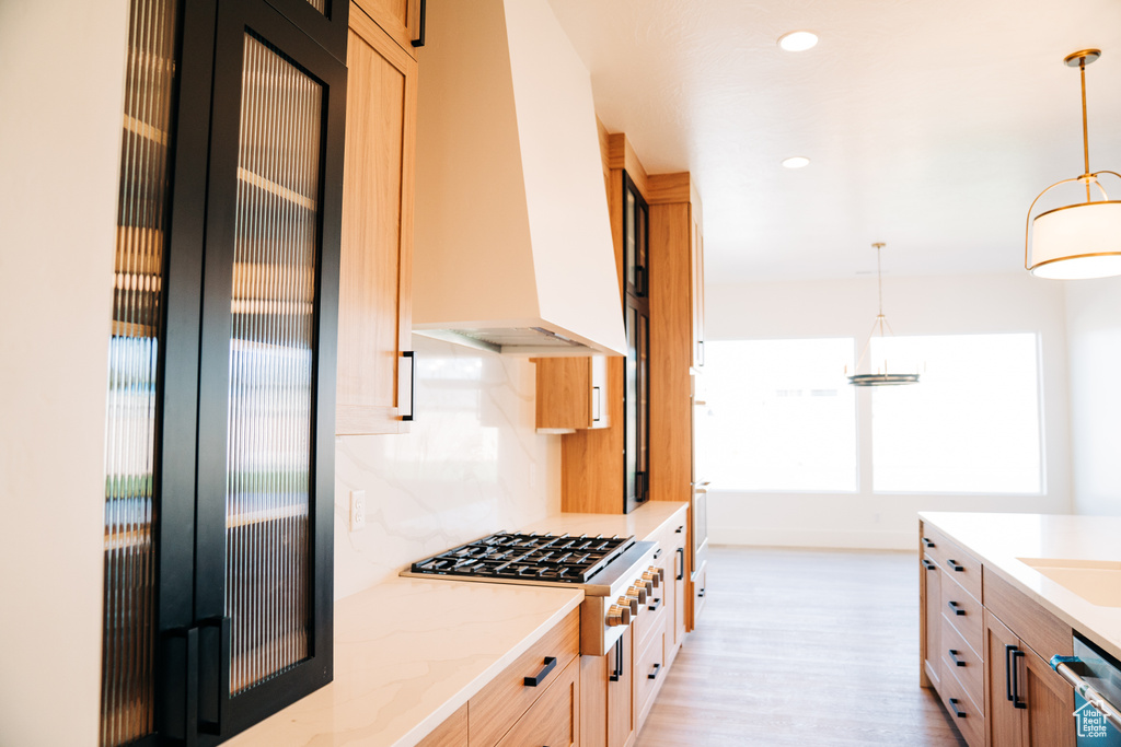 Kitchen with premium range hood, appliances with stainless steel finishes, light wood-type flooring, hanging light fixtures, and light stone countertops