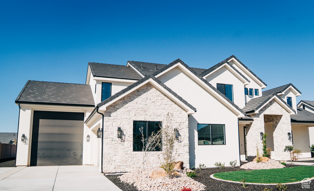 View of front of house featuring stone siding, concrete driveway, an attached garage, stucco siding, and a tiled roof