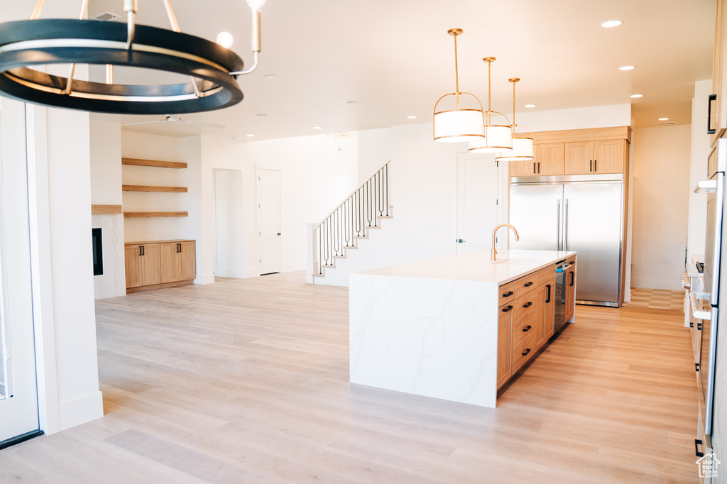 Kitchen with appliances with stainless steel finishes, light brown cabinetry, light wood-style floors, recessed lighting, and a fireplace
