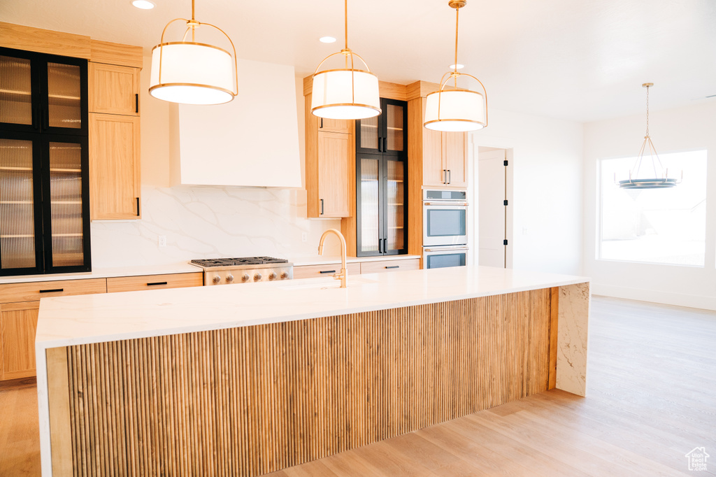 Kitchen with a sink, stainless steel appliances, light wood-type flooring, an island with sink, and light countertops