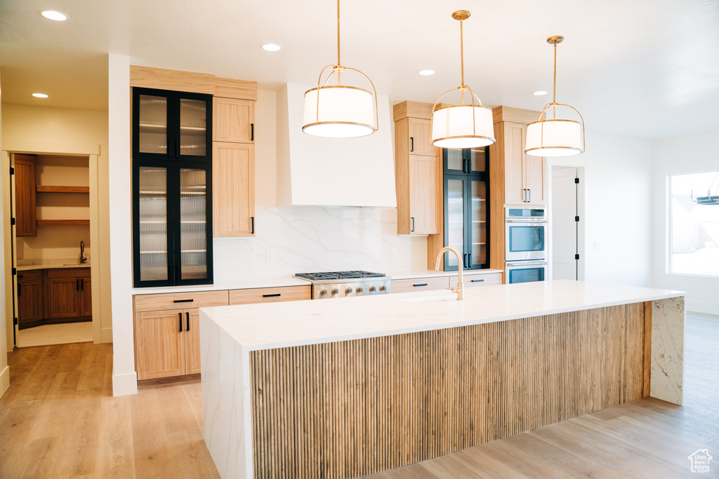 Kitchen featuring stainless steel double oven, light wood-style floors, a sink, a center island with sink, and recessed lighting