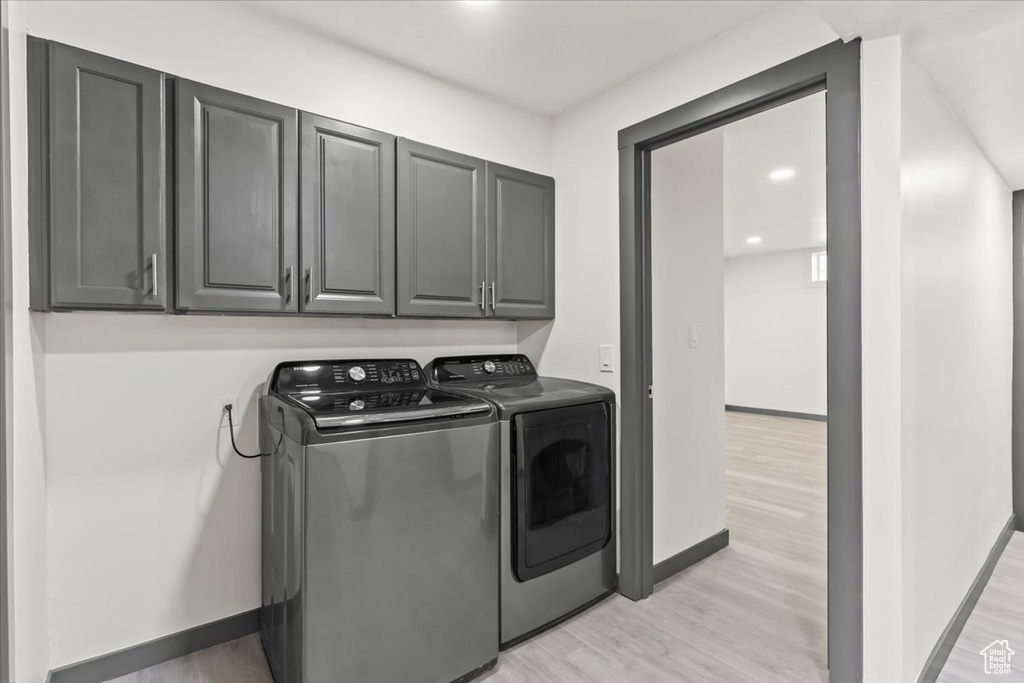 Laundry room with washer and dryer, light wood finished floors, baseboards, and cabinet space