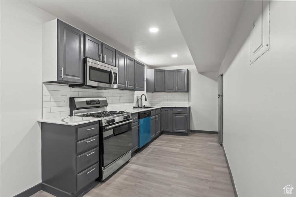Kitchen featuring stainless steel appliances, a sink, light countertops, baseboards, and light wood-style floors