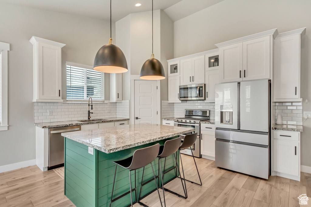 Kitchen with stainless steel appliances, a sink, white cabinetry, a kitchen island, and light stone counters