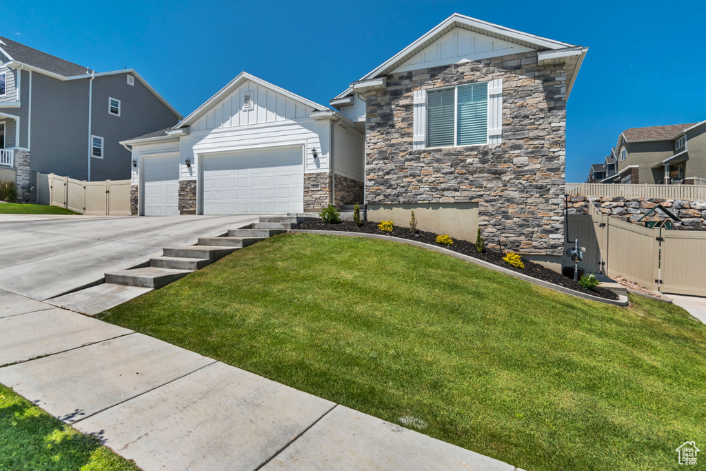 Craftsman-style house featuring stone siding, board and batten siding, driveway, an attached garage, and a gate