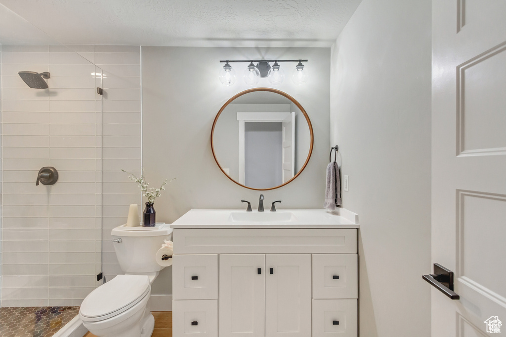 Bathroom featuring a tile shower, vanity, toilet, and a textured ceiling