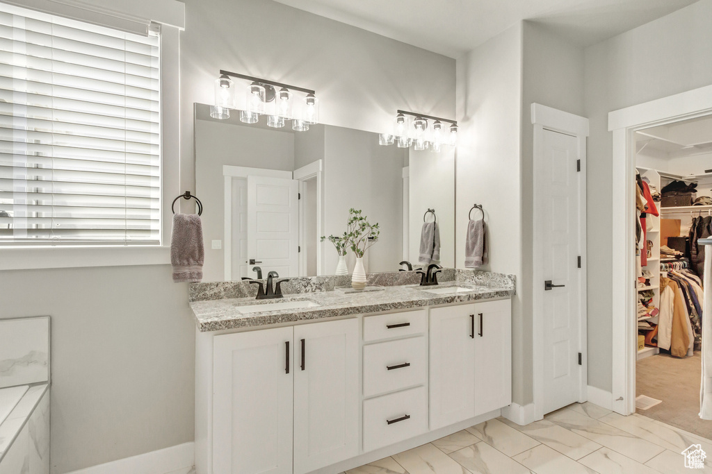 Full bathroom featuring double vanity, marble look tile flooring, a spacious closet, and baseboards