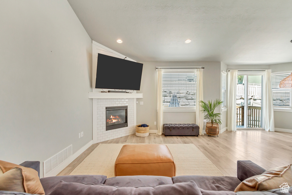 Living room with light wood-type flooring, plenty of natural light, a glass covered fireplace, baseboards, and recessed lighting