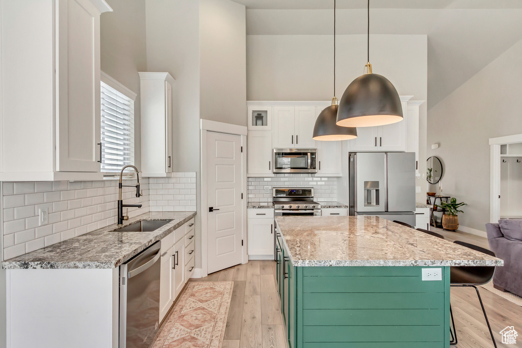 Kitchen featuring stainless steel appliances, a sink, high vaulted ceiling, white cabinets, and a center island