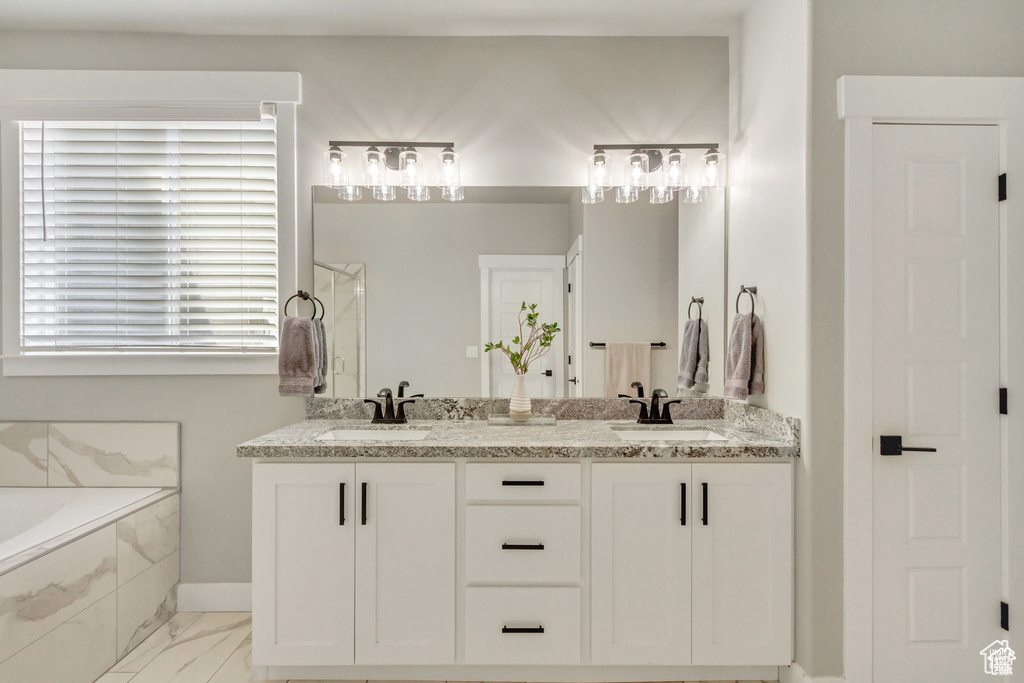 Bathroom with a bath, double vanity, baseboards, a shower with door, and marble look tile flooring