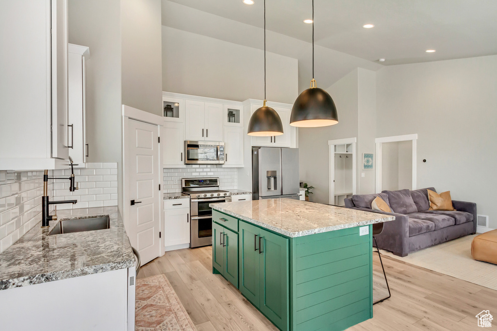 Kitchen featuring stainless steel appliances, high vaulted ceiling, a sink, white cabinetry, and light wood finished floors