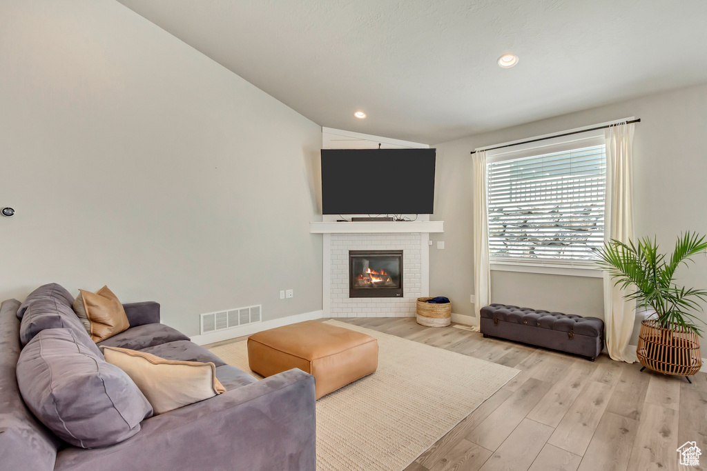 Living area featuring light wood-style flooring, lofted ceiling, baseboards, a fireplace, and recessed lighting