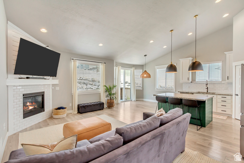 Living room with vaulted ceiling, light wood-style flooring, plenty of natural light, a fireplace, and recessed lighting