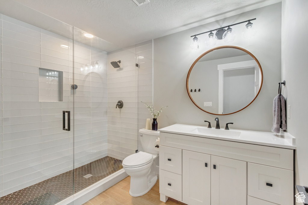 Bathroom featuring wood finished floors, a shower stall, vanity, toilet, and a textured ceiling