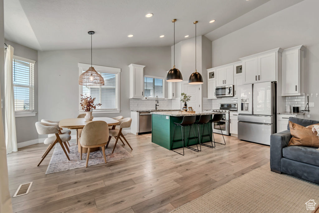 Kitchen featuring appliances with stainless steel finishes, a kitchen breakfast bar, white cabinets, backsplash, and a kitchen island