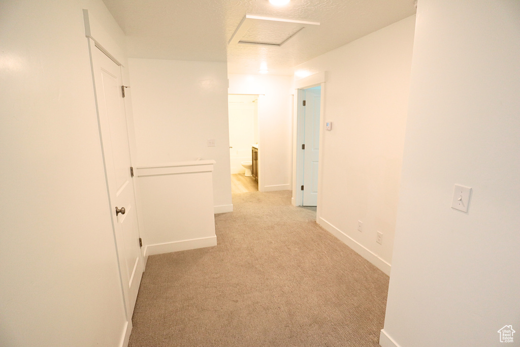 Corridor with baseboards, attic access, and light colored carpet