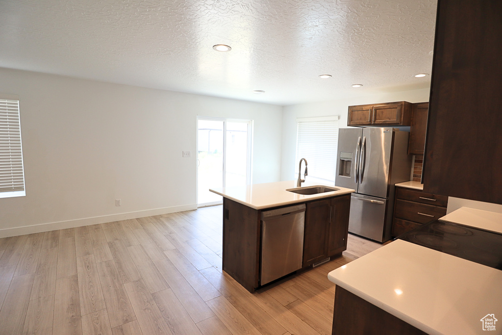 Kitchen featuring appliances with stainless steel finishes, a sink, a kitchen island with sink, a textured ceiling, and light wood-type flooring