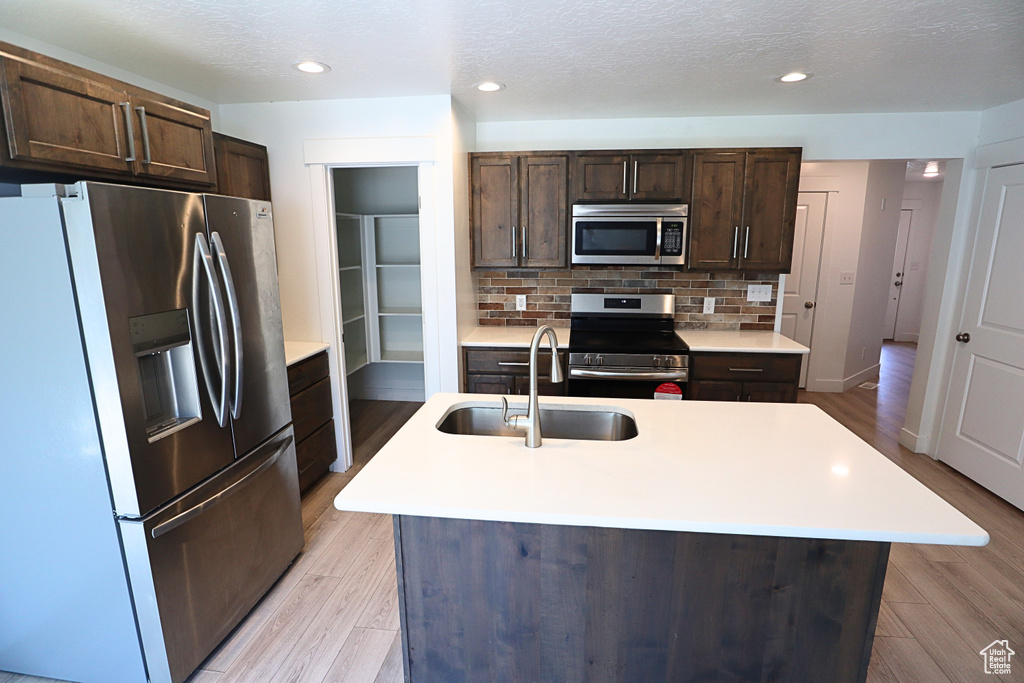 Kitchen with stainless steel appliances, a sink, dark brown cabinets, light countertops, and recessed lighting