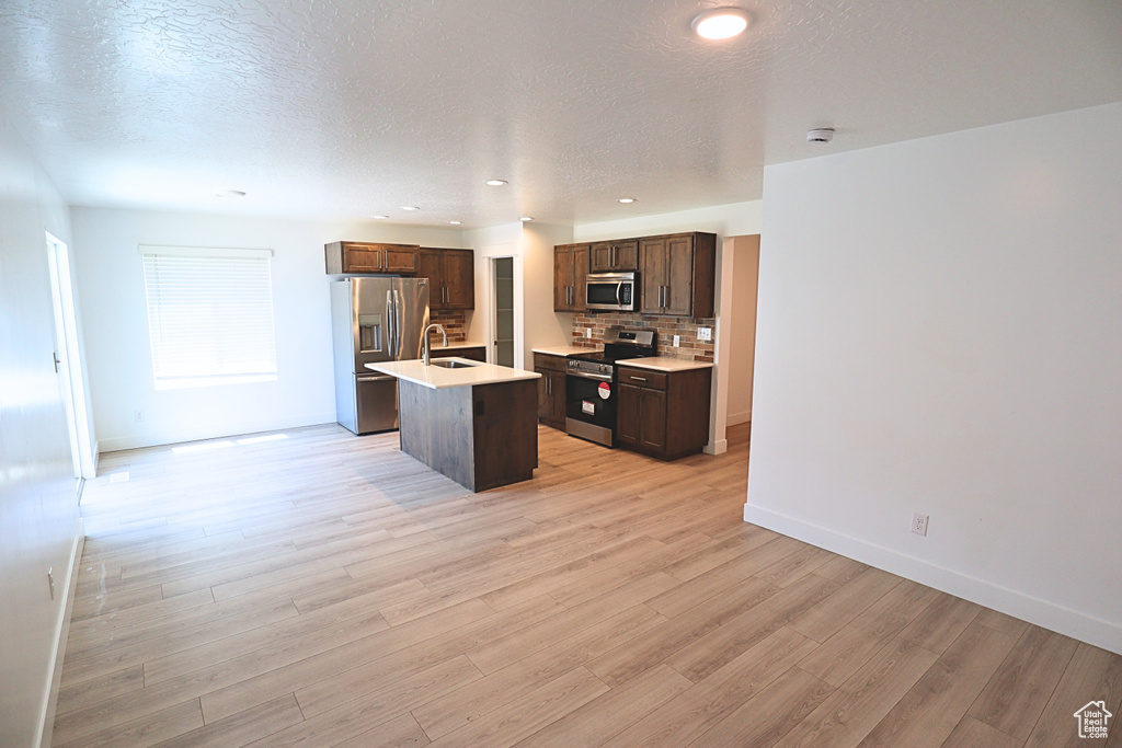 Kitchen with stainless steel appliances, a sink, dark brown cabinetry, light countertops, and an island with sink