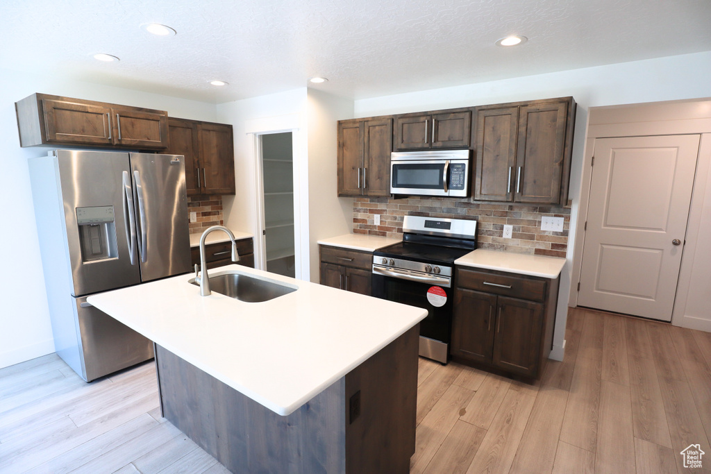 Kitchen with appliances with stainless steel finishes, a sink, light wood finished floors, light countertops, and dark brown cabinets