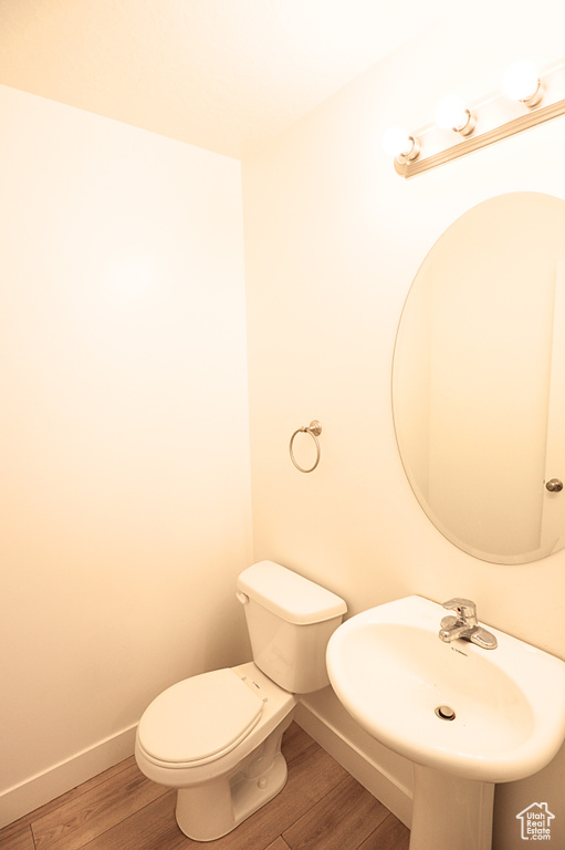 Half bath with wood finished floors, toilet, baseboards, and a sink