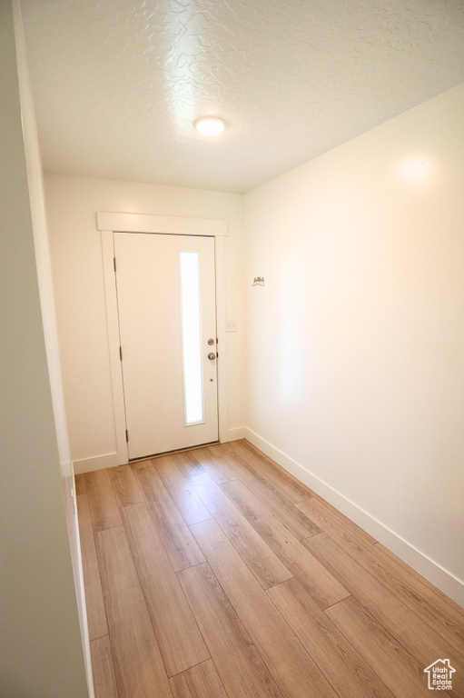 Entrance foyer with baseboards, light wood-style floors, and a textured ceiling