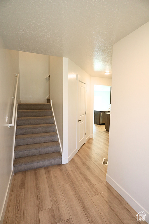 Stairway with wood finished floors, baseboards, and a textured ceiling