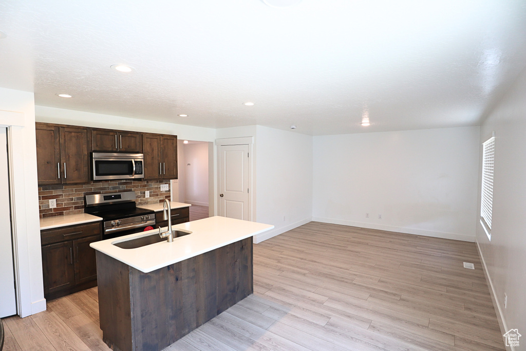 Kitchen featuring stainless steel appliances, a sink, tasteful backsplash, light wood-style floors, and dark brown cabinets