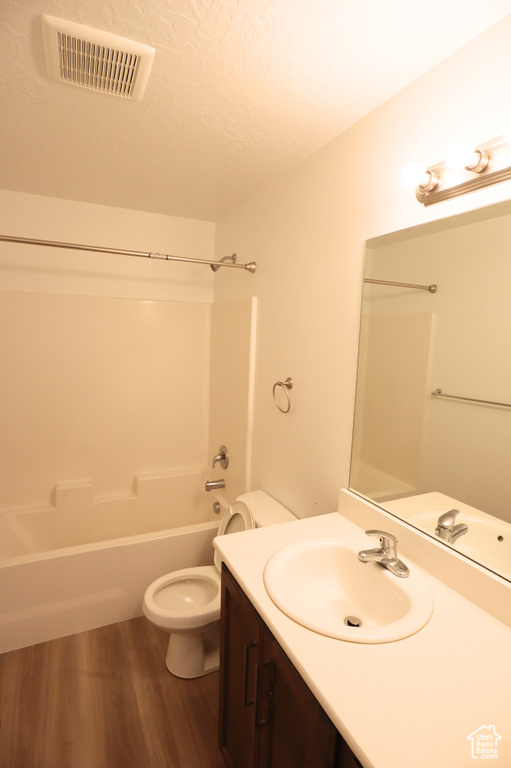 Bathroom featuring toilet, vanity, bathing tub / shower combination, wood finished floors, and a textured ceiling