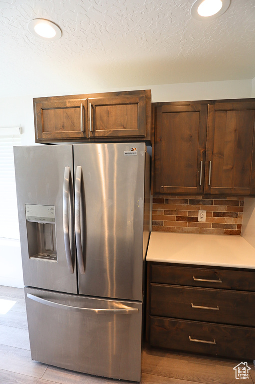 Kitchen with stainless steel refrigerator with ice dispenser, light countertops, backsplash, wood finished floors, and a textured ceiling
