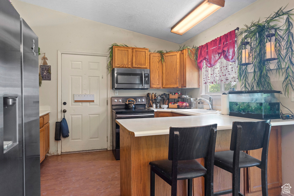 Kitchen with appliances with stainless steel finishes, a sink, a peninsula, brown cabinets, and light countertops