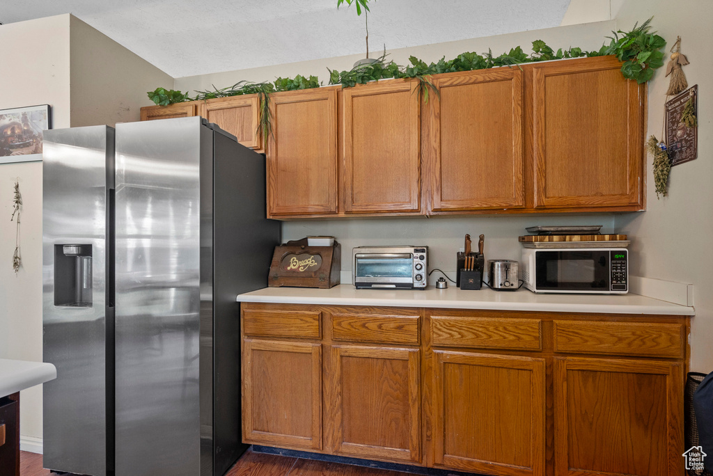 Kitchen with stainless steel fridge with ice dispenser, black microwave, light countertops, and dark wood-style floors