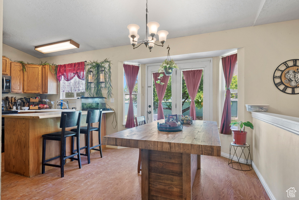 Kitchen featuring light wood-style flooring, stainless steel microwave, brown cabinetry, a chandelier, and plenty of natural light