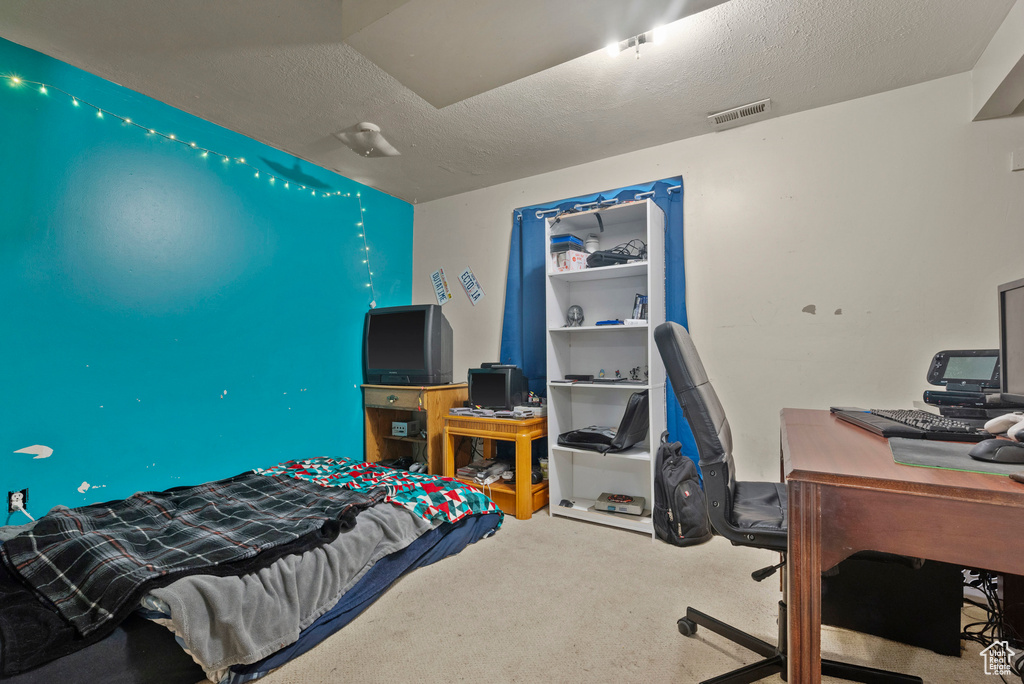Carpeted bedroom featuring an office area and a textured ceiling