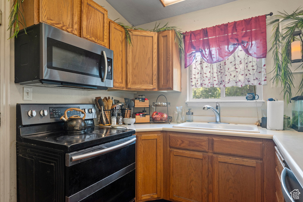 Kitchen with range with two ovens, stainless steel microwave, a sink, light countertops, and brown cabinets