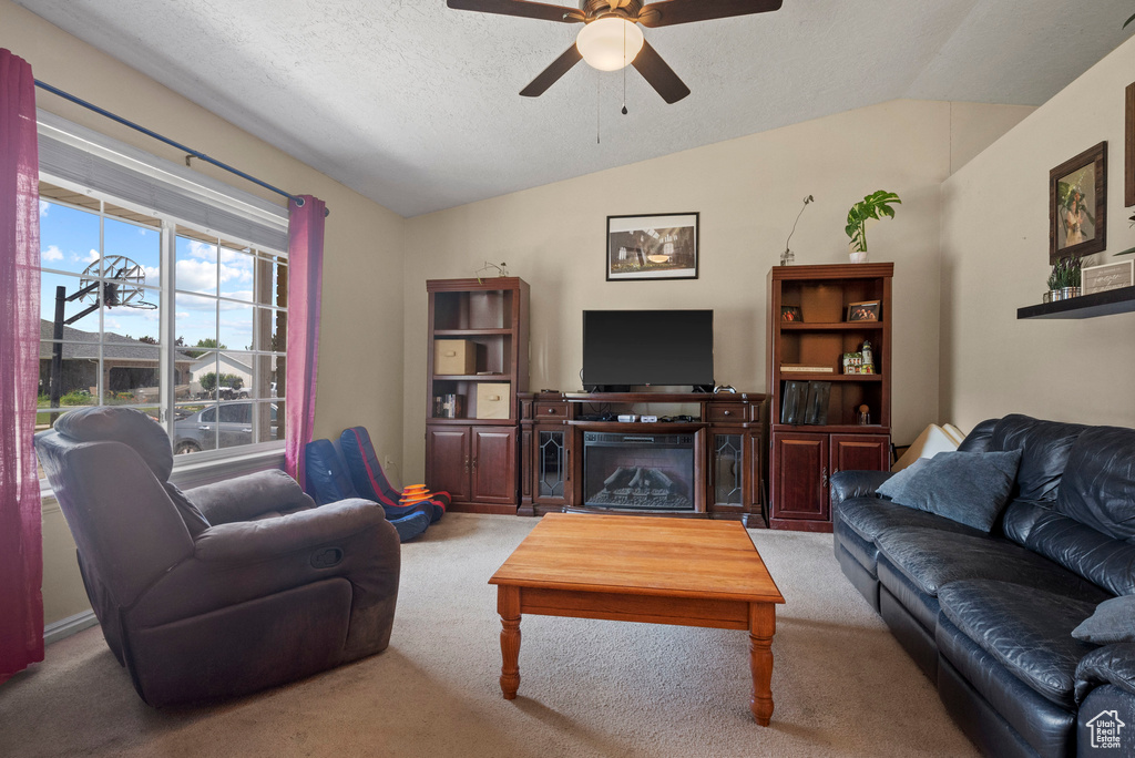 Living room with lofted ceiling, ceiling fan, carpet, a textured ceiling, and a glass covered fireplace